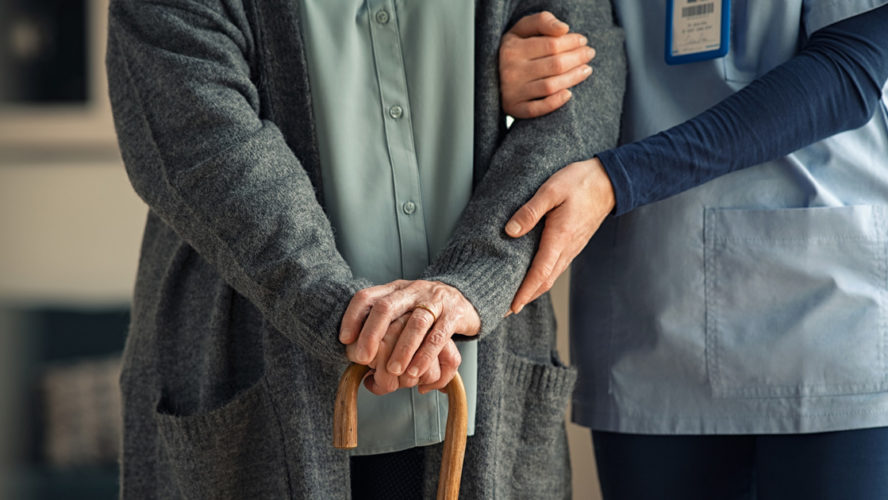 Close up hands of caregiver doctor helping old woman at private clinic. Close up of hands of nurse holding a senior patient with walking stick. Elder woman using walking cane at nursing home with nurse holding hand for support.