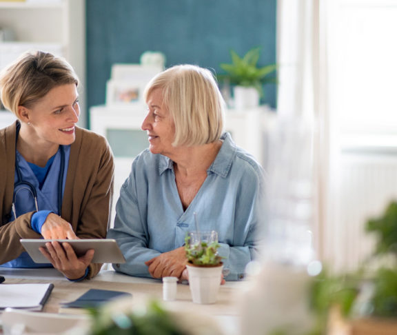 Caregiver or healthcare worker with senior woman patient, using tablet and explaining.