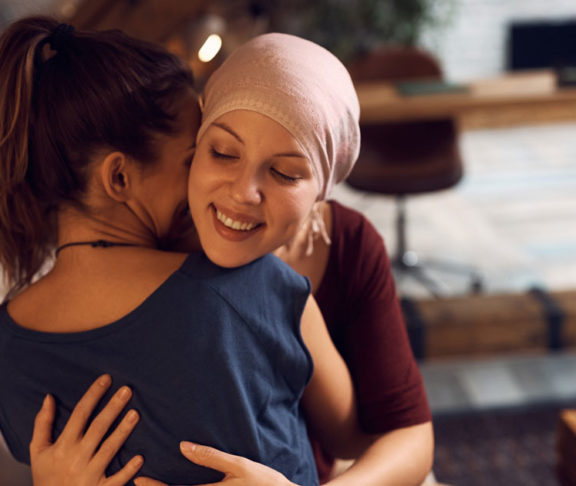 Happy cancer patient embracing her friend who is visiting her at home.