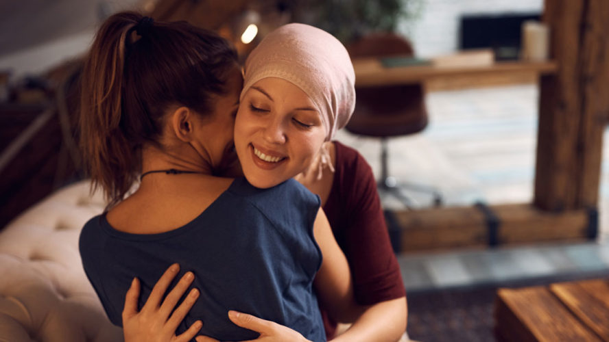 Happy cancer patient embracing her friend who is visiting her at home.