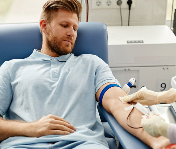 Portrait of handsome young man preparing for blood donation at med center with nurse helping