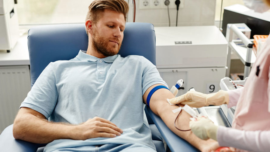 Portrait of handsome young man preparing for blood donation at med center with nurse helping