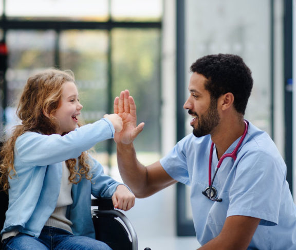 Young multiracial doctor having fun with little girl on wheelchair