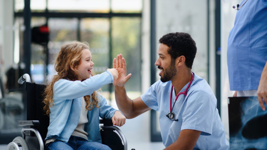 Young multiracial doctor having fun with little girl on wheelchair