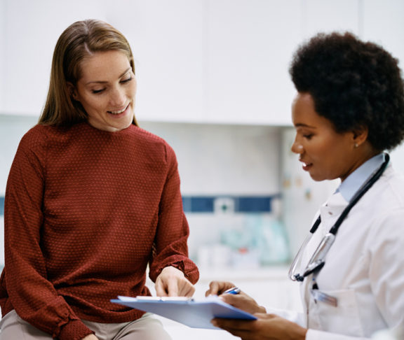 African American doctor and her female patient analyzing medical report after examination in the hospital. Focus is on female patient.