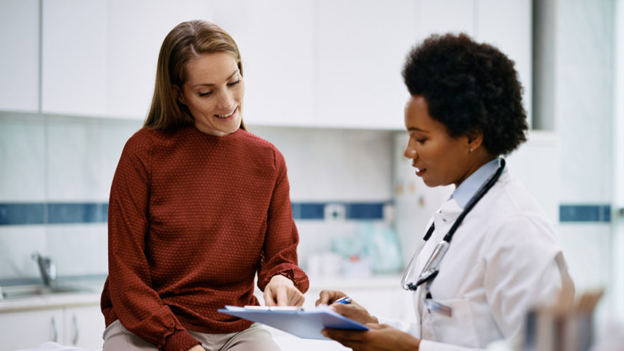 African American doctor and her female patient analyzing medical report after examination in the hospital. Focus is on female patient.