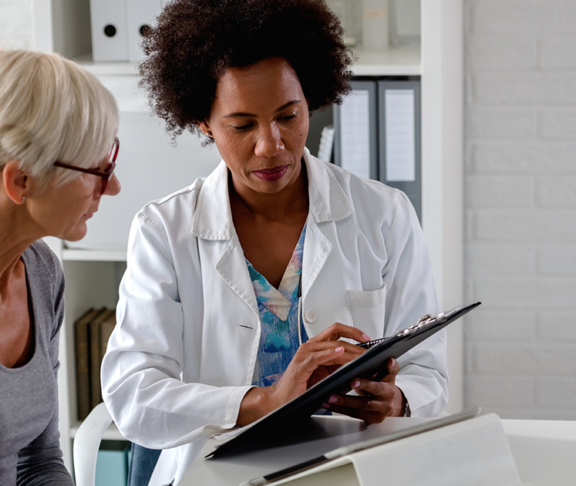 A female doctor sits at her desk and chats to an elderly female patient while looking at her test results