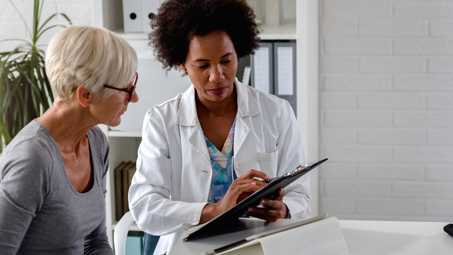 A female doctor sits at her desk and chats to an elderly female patient while looking at her test results