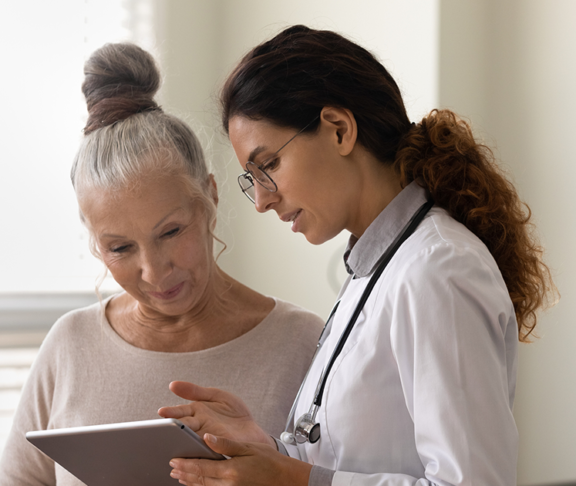 Serious GP doctor showing tablet screen to old female patient