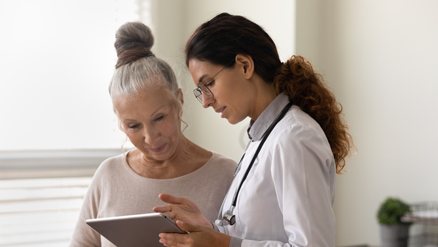 Serious GP doctor showing tablet screen to old female patient